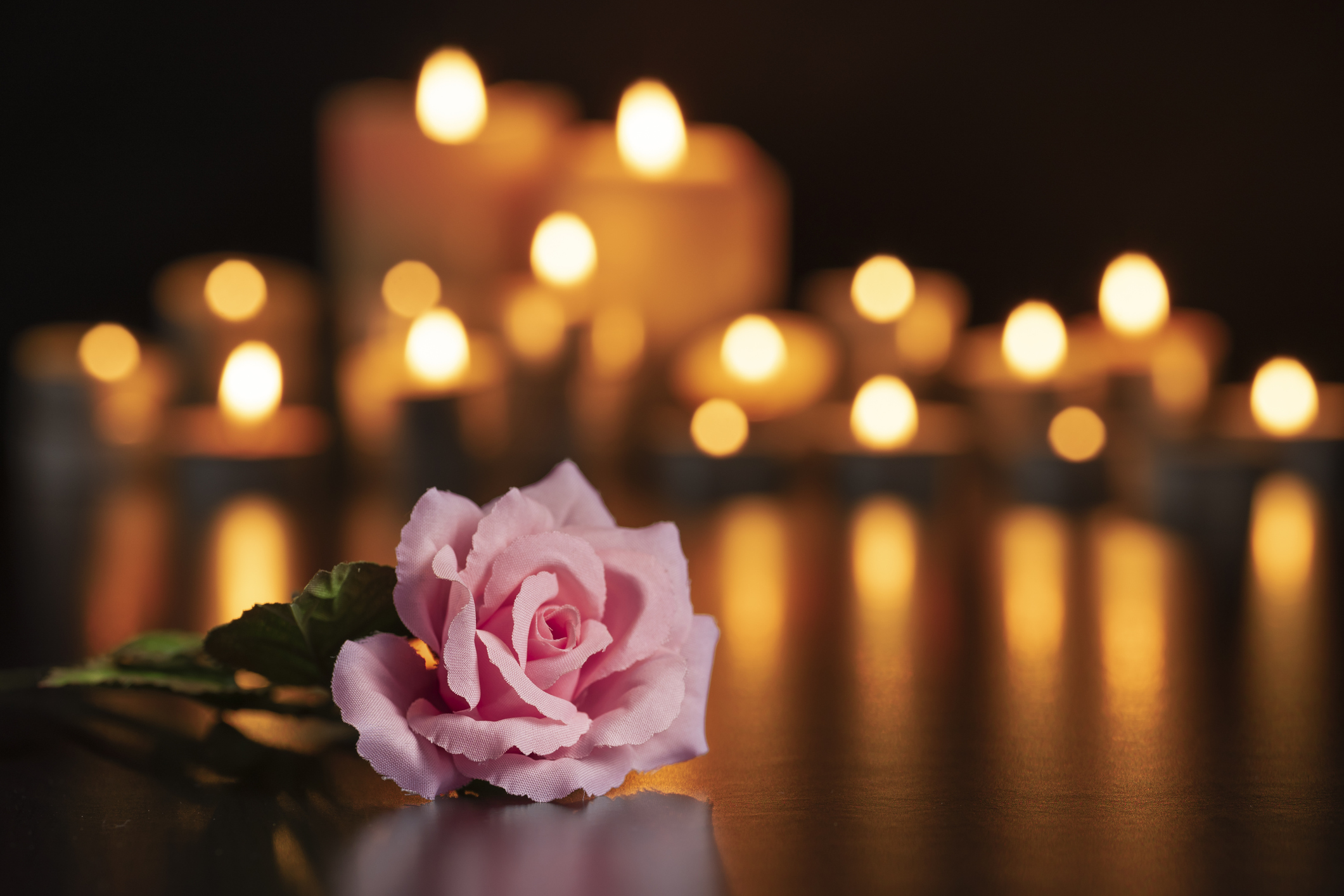 Pöydällä vaaleanpunainen ruusu, taustalla kynttilöitä.