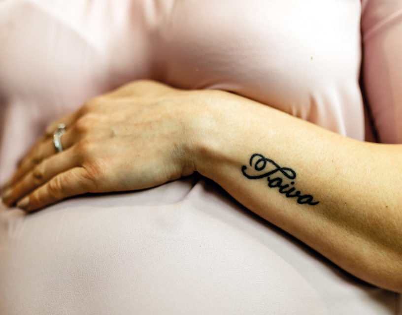 Hand håller om gravid mage, namnet Toivo tatuerat på armen.