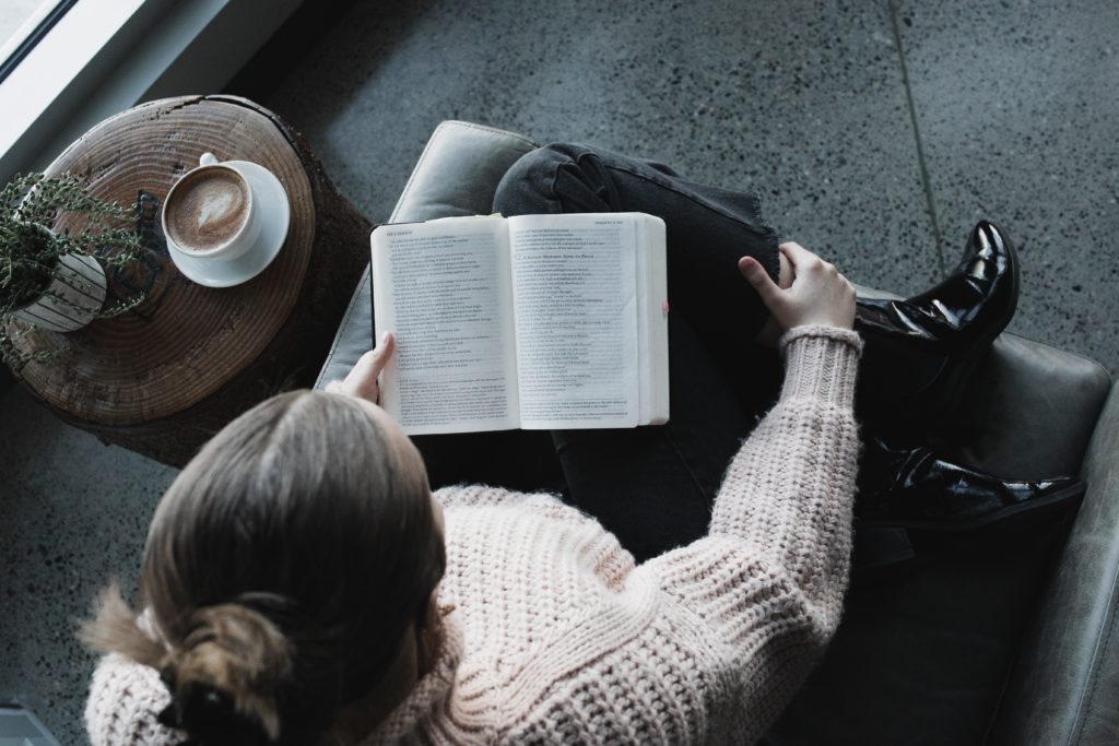 Nainen lukee Eaamattua kahvikupin äärellä.