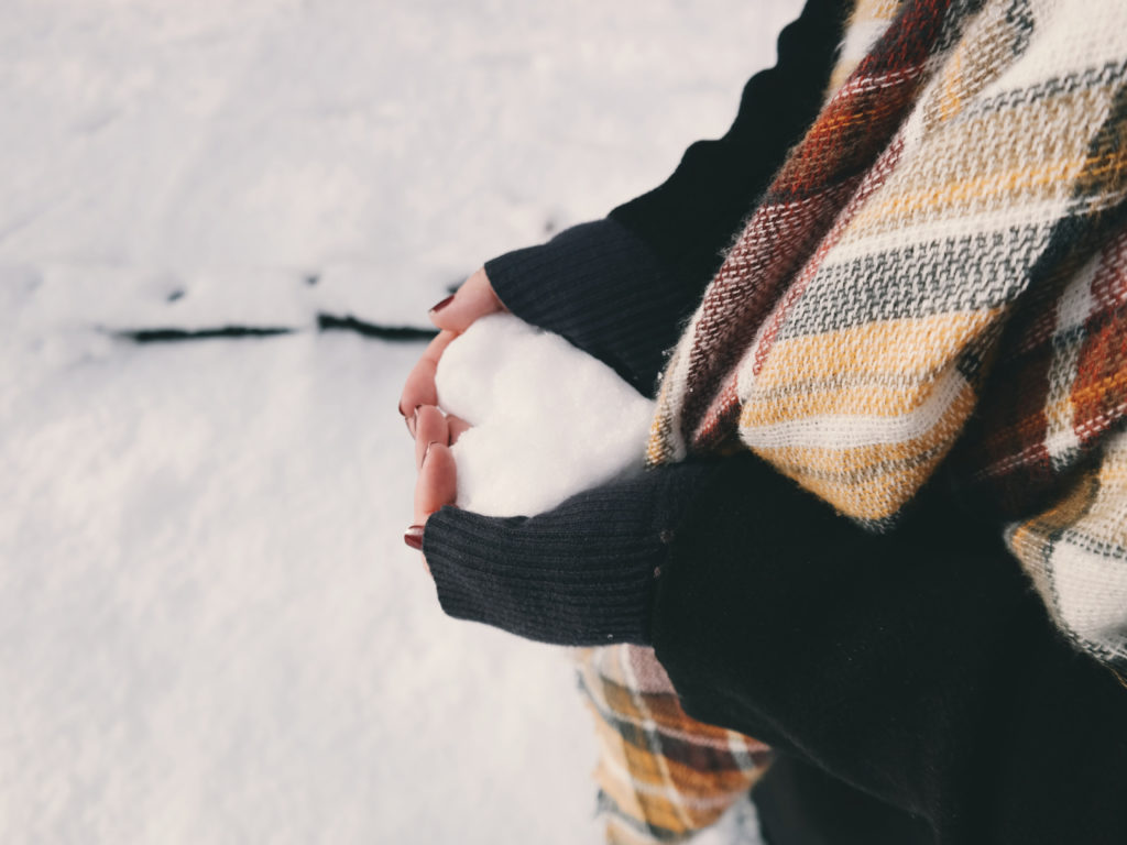 En människa håller ett hjärta format av snö i kupade händer i höjd med sin mage.
