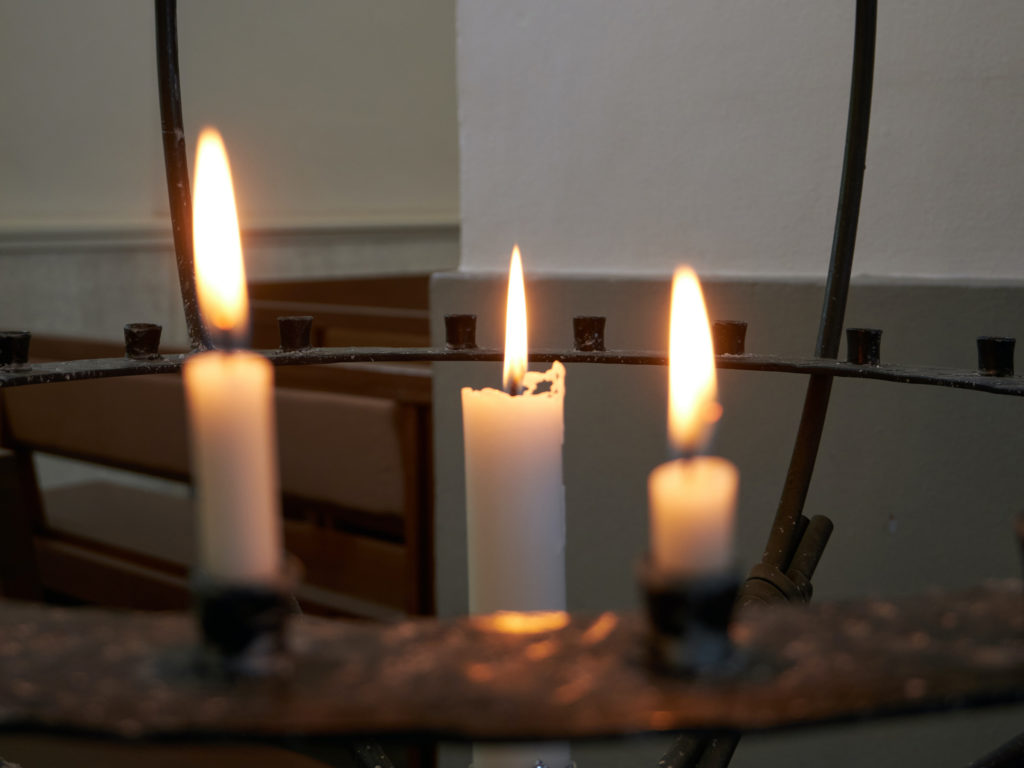 Tre stearinljus brinner i en ljusglob i kyrkan.