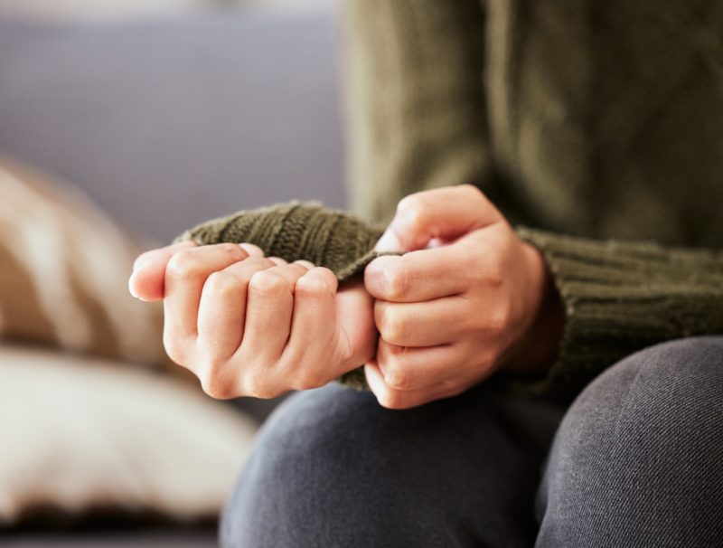 Person sitter och drar nervöst i sin tröjärm.