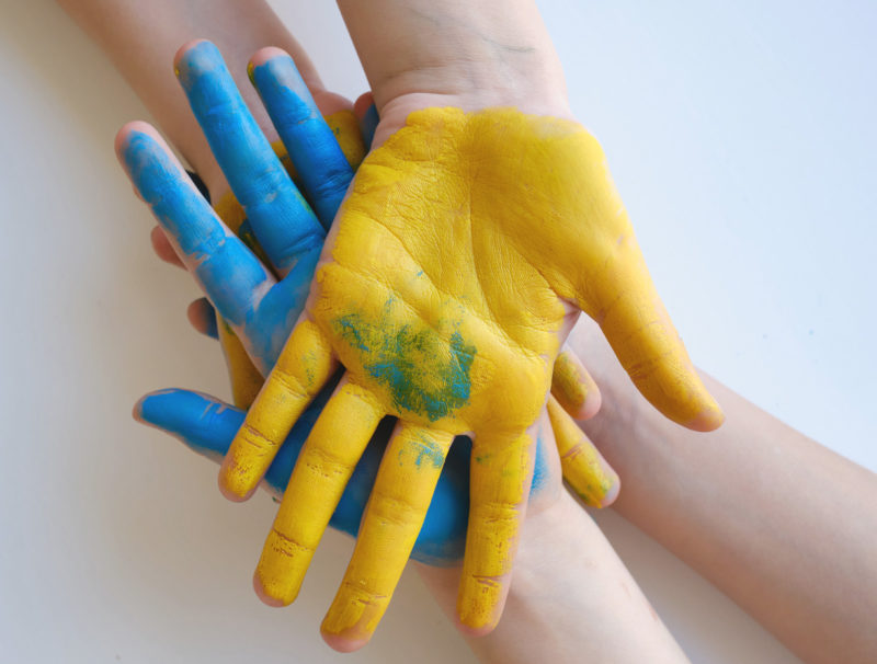 Händer med handflatorna målade i gult respektive blått.