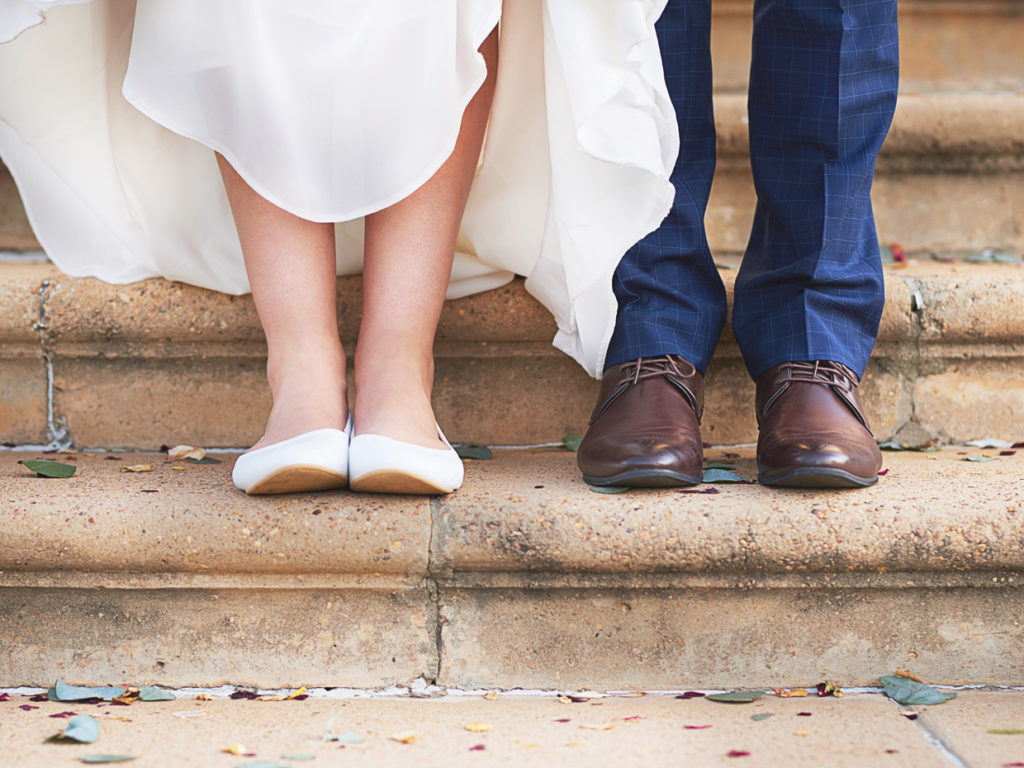 Närbild på fötterna på ett brudpar som står på stentrappor.