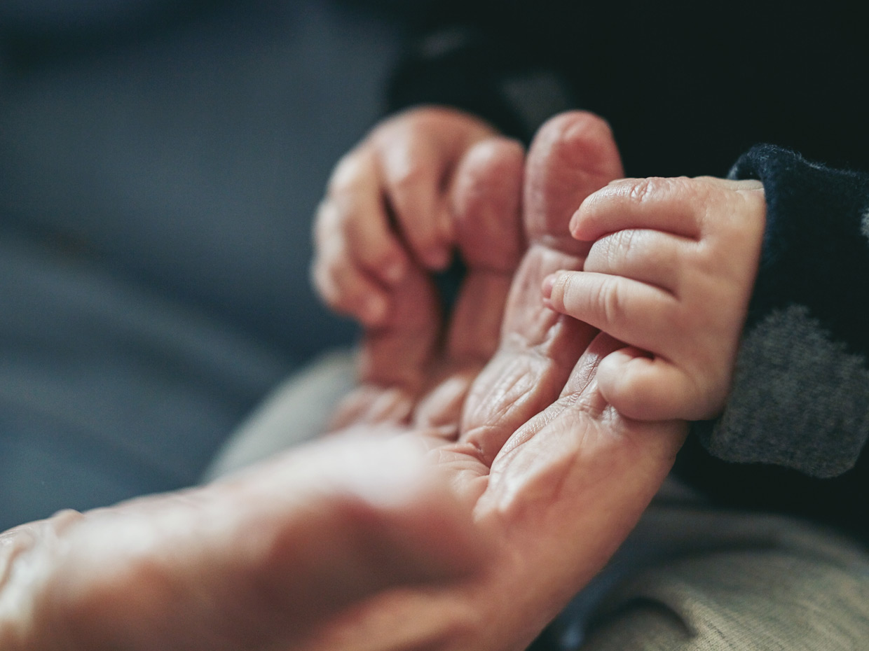 En babys små händer som griper tag i en äldre människas rynkiga fingrar.