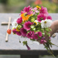 Människa lägger ner bukett med sommarblommor vid en grav.