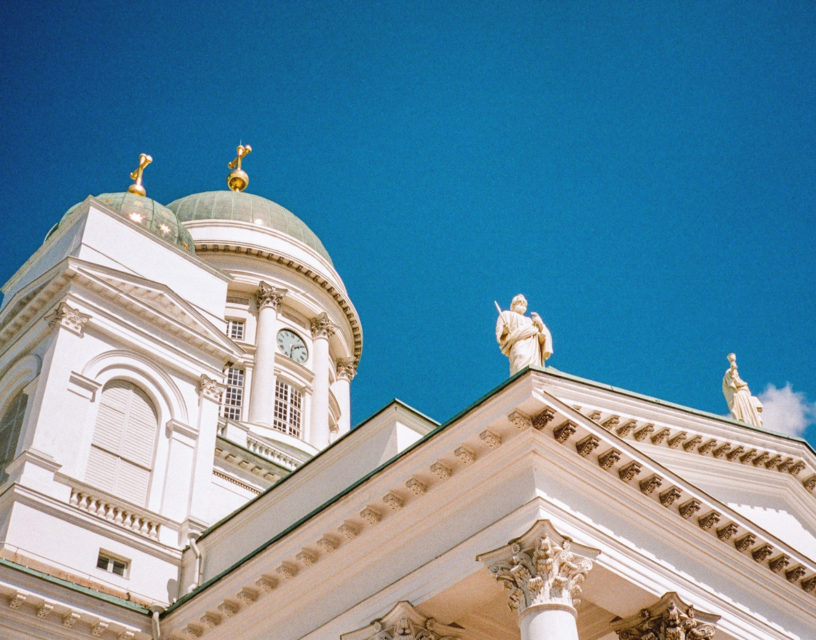 En kyrkas vita väggar och gröna takkupoler mot en klarblå himmel.