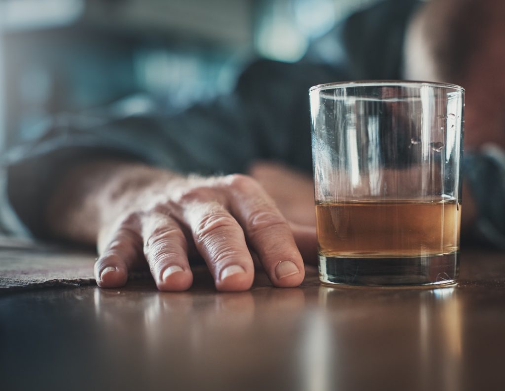 En hand vilar på ett bord bredvid ett glas med alkohol.