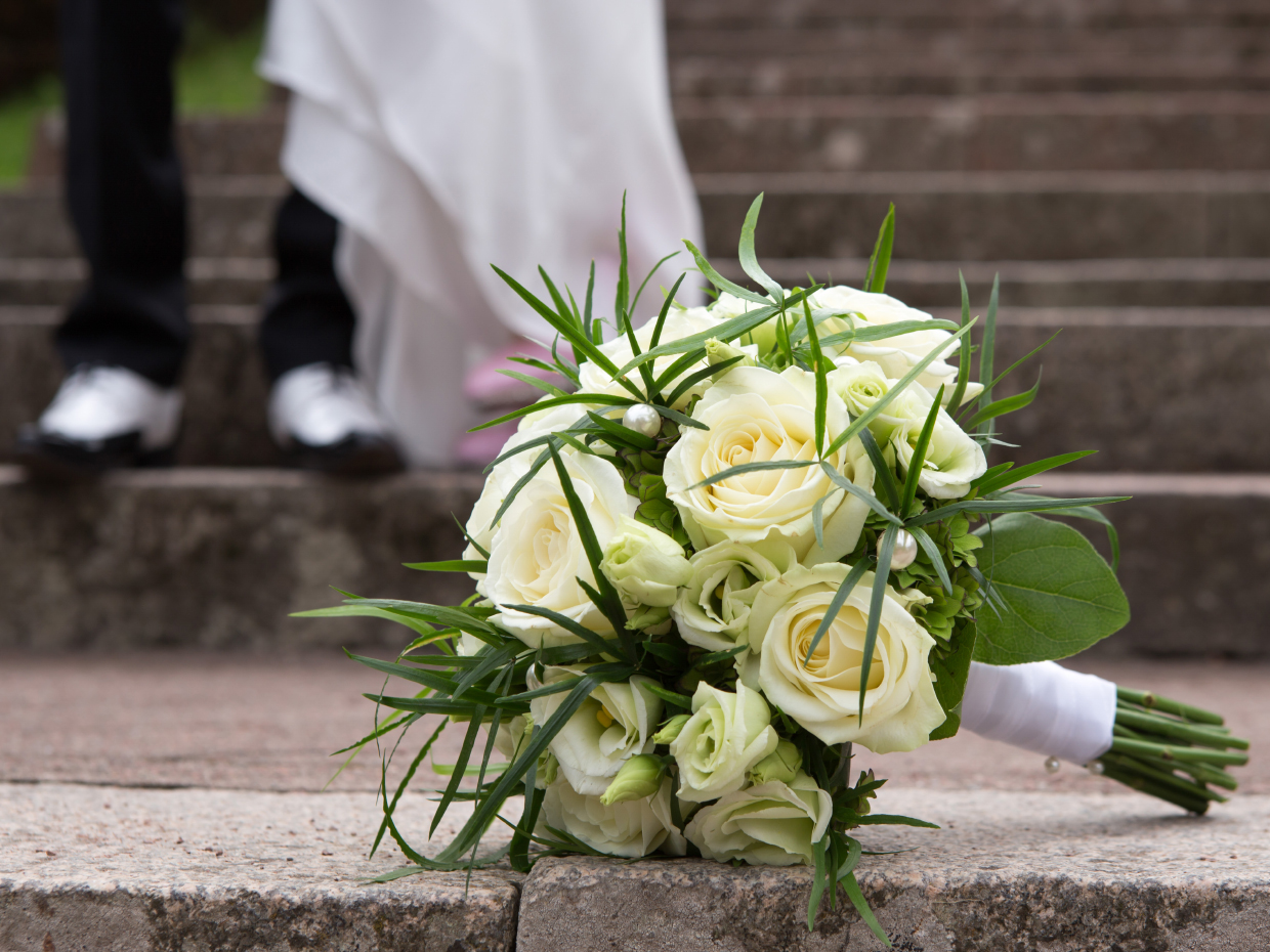 En brudbukett ligger på kyrktrappan, i bakgrunden skymtar en vit klänning.
