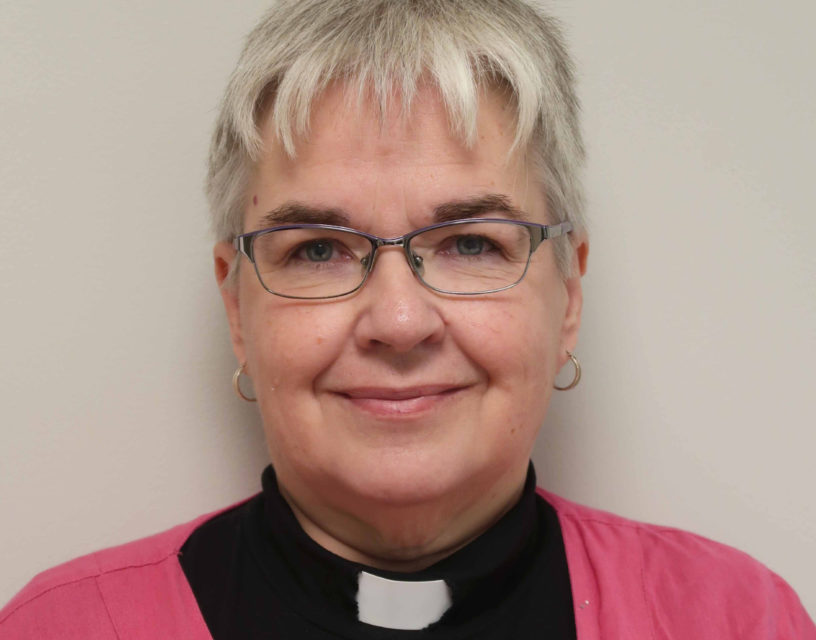 Porträttbild på kvinna med prästskjorta, kort, grått hår och glasögon.