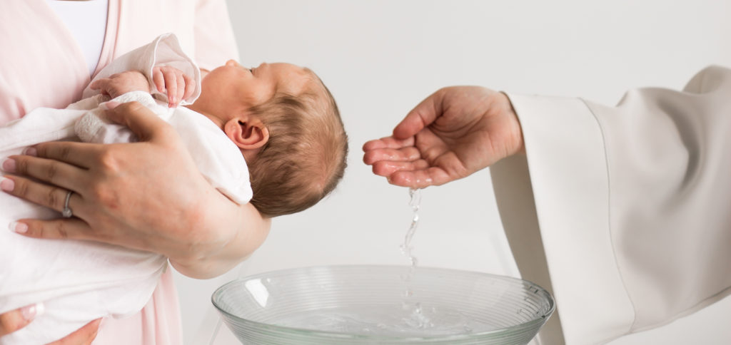 Prästen sätter vatten från dopskålen på babyns huvud.