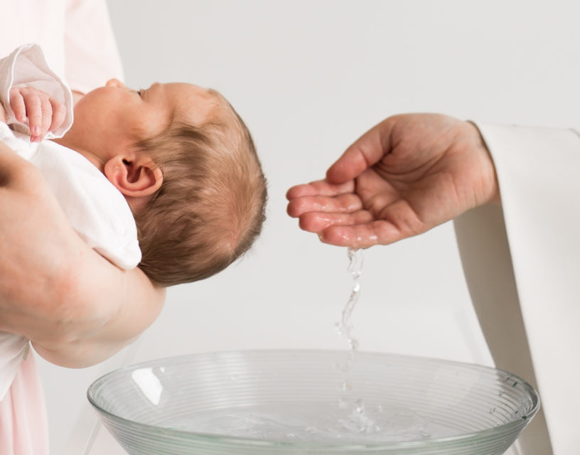 Prästen sätter vatten från dopskålen på babyns huvud.