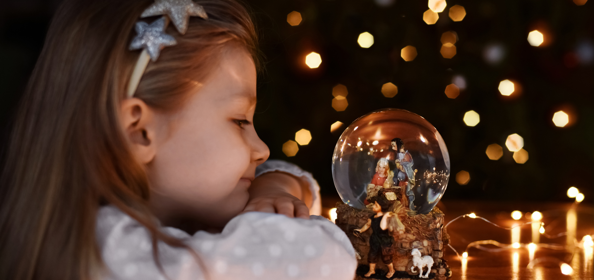 Flicka tittar på en snöglob med en julkrubba i.