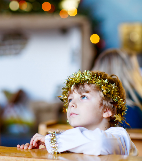 Ett barn med vit dräkt och gulglitter i håret sitter i kyrkbänk.