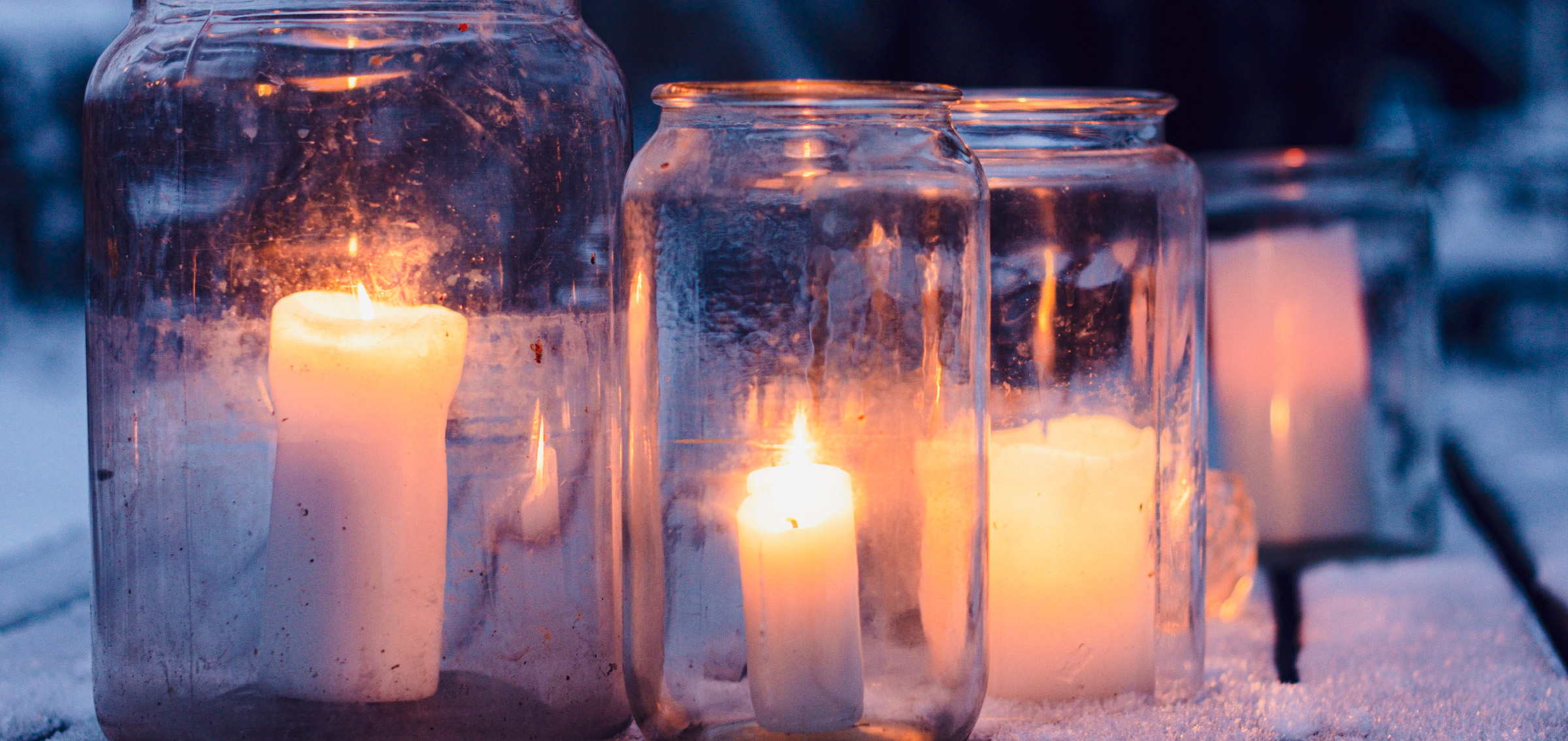 Glasbrukar med brinnande ljus på ett snötäckt trädgårdsbord.