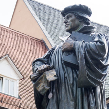 Bronsstaty av reformatorn Martin Luther, hustak i bakgrunden.