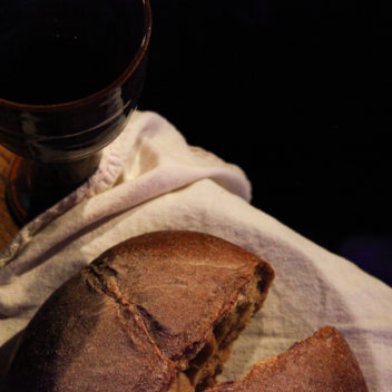 Ett brutet bröd och en bägare med vin på en vit duk.