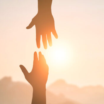 Kaksi toisiaan kohti kurkottavaa kättä auringonpaisteessa.