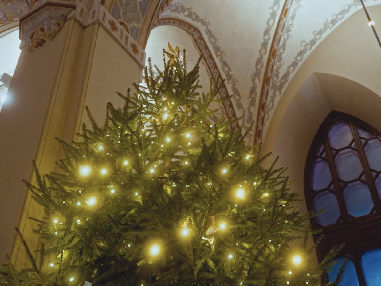 En julgran med klara ljus står i en kyrka.