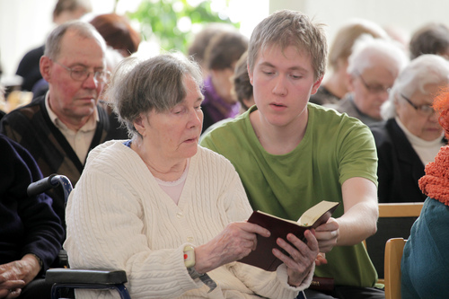 A young man reading a book with an elderly lady.