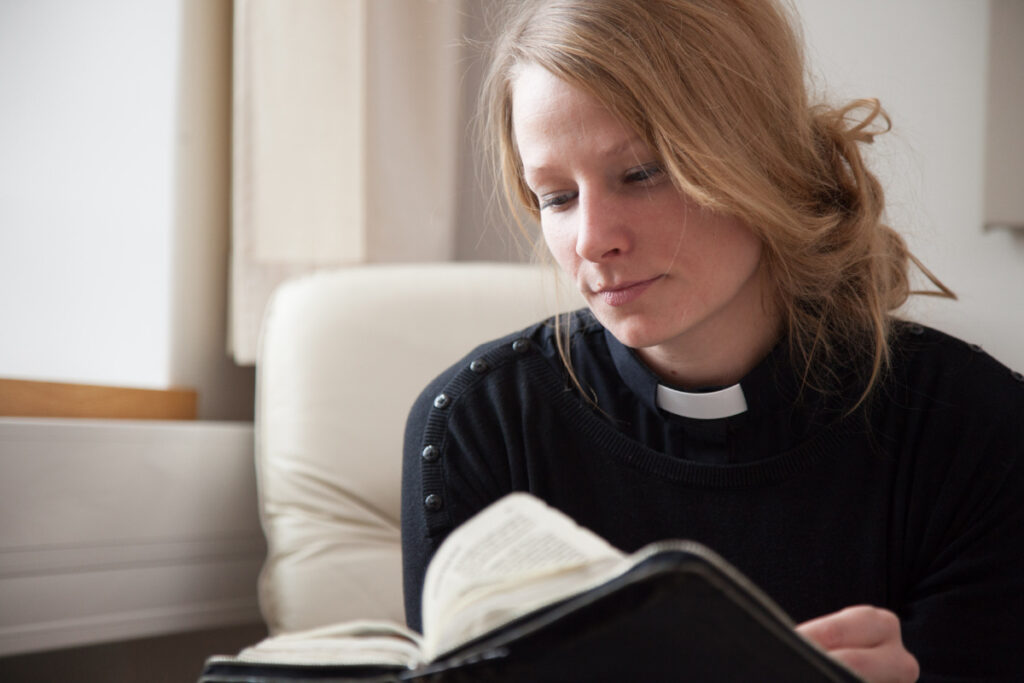 Ung kvinna med prästskjorta och svart tröja bläddrar i bibel.