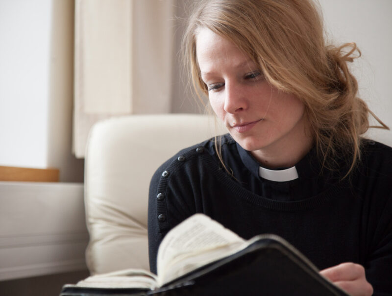 Naispuolinen pappi selaa raamattua.