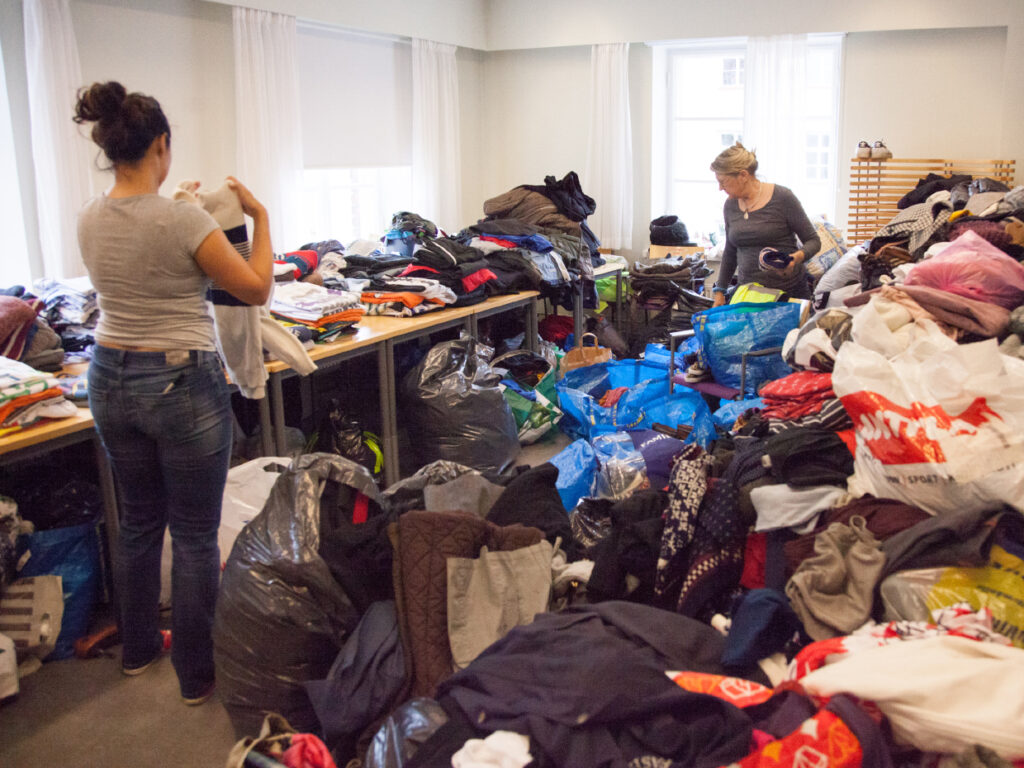 Två personer arbetar med att sortera högar av donerade kläder.
