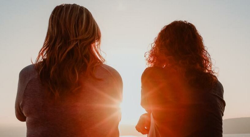 Kaksi ihmistä istuu selin katsomassa auringonlaskua