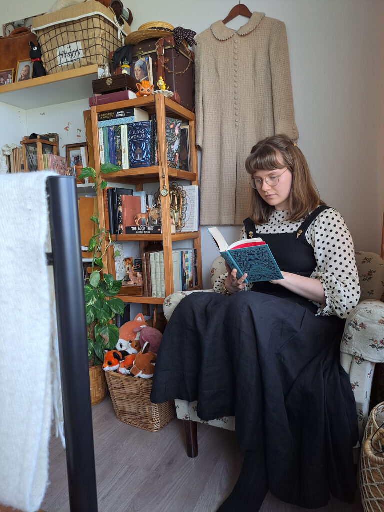 Kvinna sitter i fåtölj i lägenhet och läser bok.