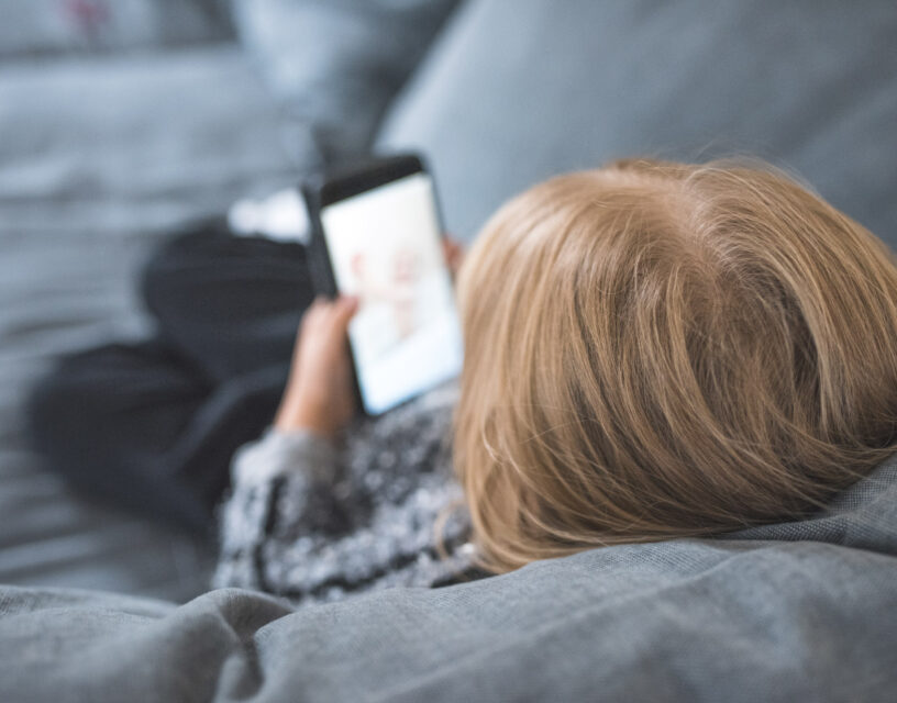 En person ligger i en soffa och skrollar på telefonen.