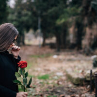 Nuori nainen hautausmaalla ruusu kädessään.