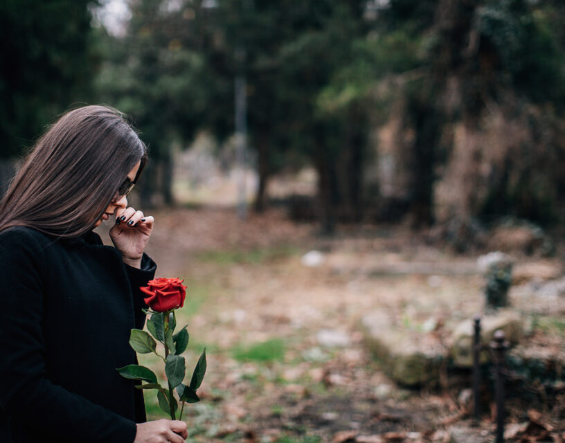 Nuori nainen hautausmaalla ruusu kädessään.