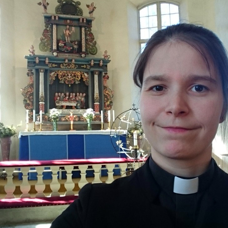 Selfie på kvinna i prästkrage, i bakgrunden altaret i en kyrka.