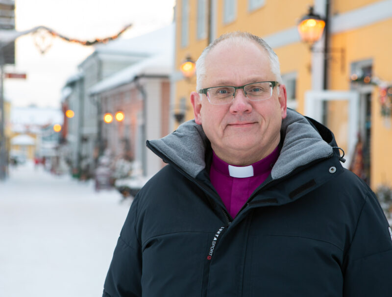 Biskop Bo-Göran Åstrand står på en gata i Borgås gamla stad. Bakom honom syns julljus.