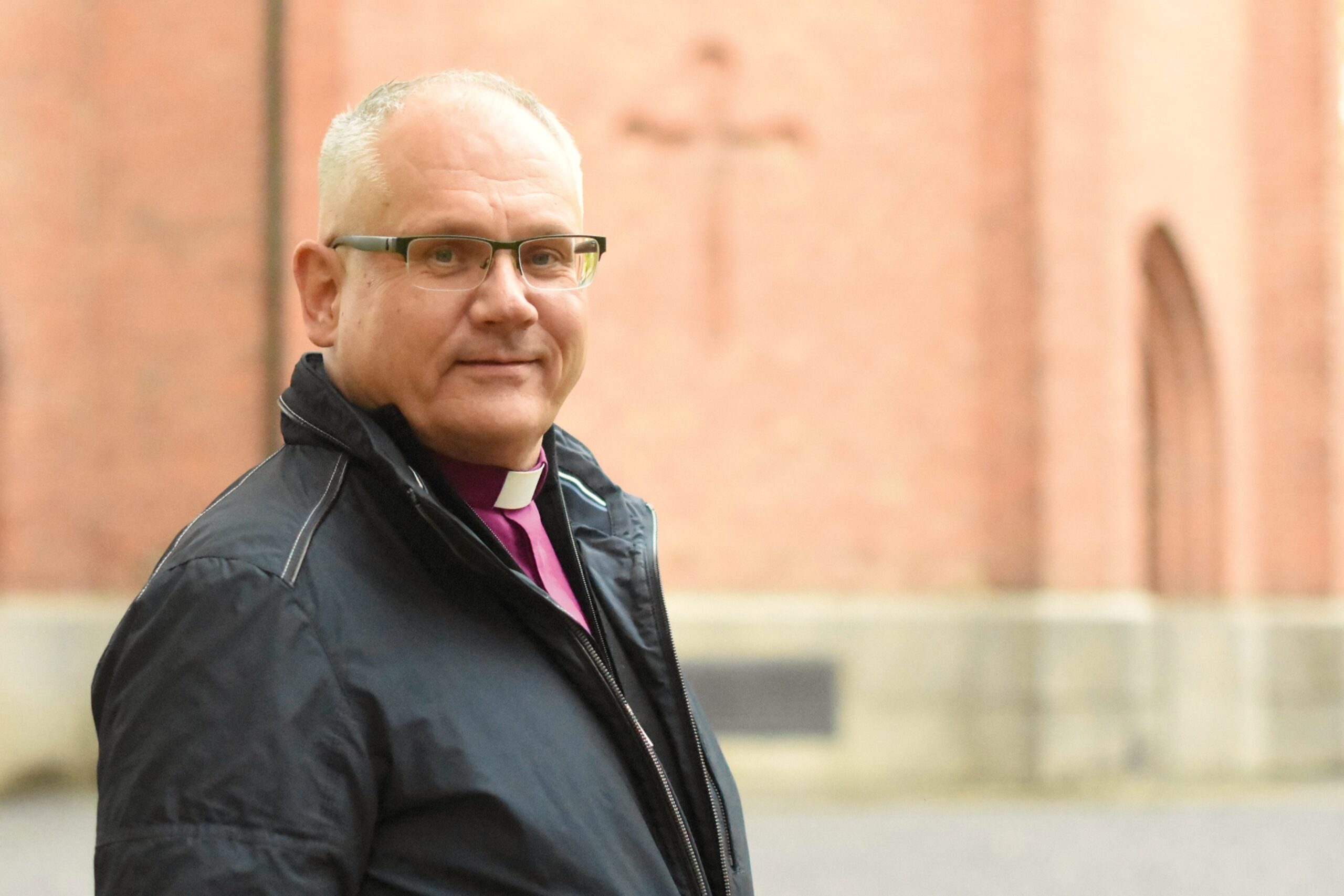 Biskop Bo-Göran Åstrand står framför en kyrkvägg. Han har på sig en svart jacka över biskopsskjortan.