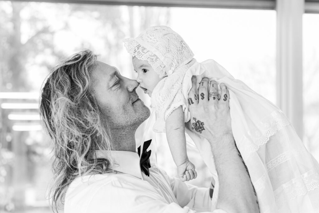 Jukka Hildén håller en bebis klädd i en dopklänning i sin famn.
