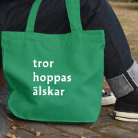 Människa med en grön tygkasse med trycket "tror hoppas älskar".