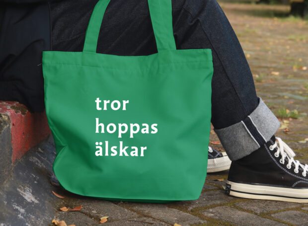 Människa med en grön tygkasse med trycket "tror hoppas älskar".