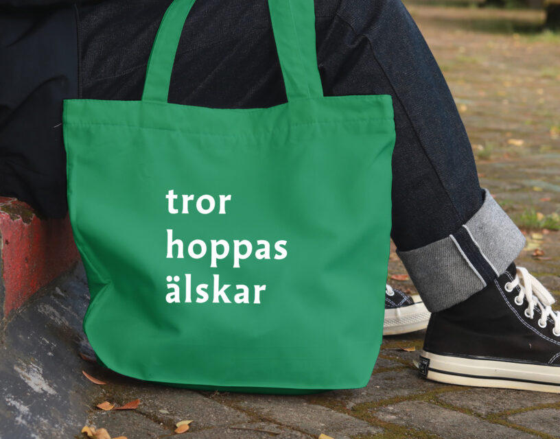 Människa med en grön tygkasse med trycket "tror hoppas älskar".